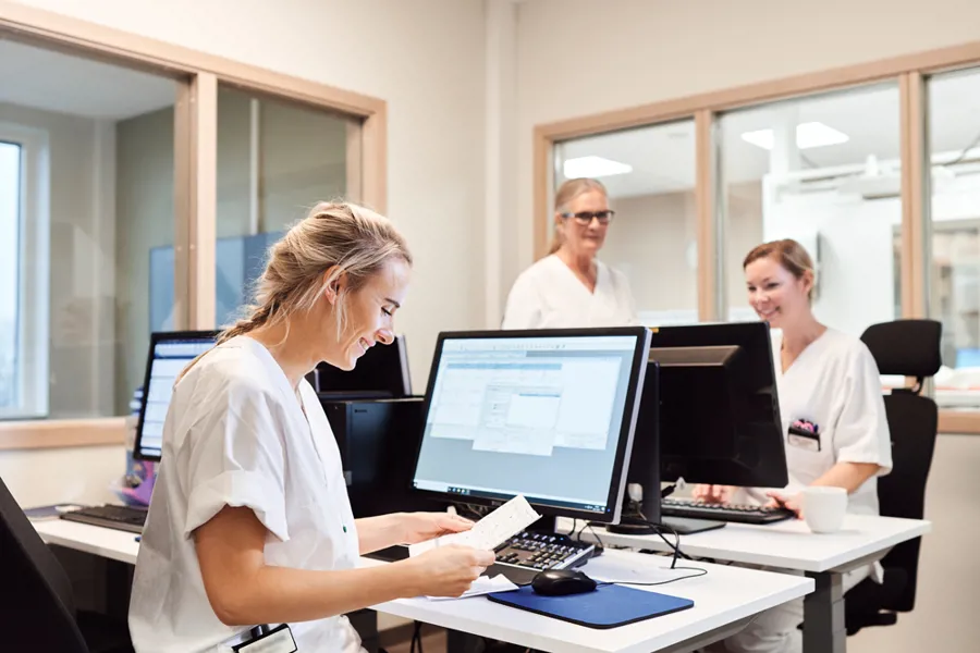 Tre sykepleiere som jobber på et kontor foran datamaskiner