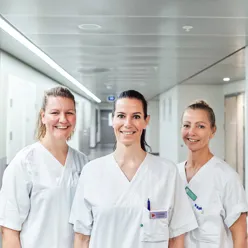 Tre smilende, kvinnelige sykepleiere i hvitt arbeidsantrekk