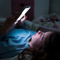 En kvinne som ligger i sengen med mobiltelefon